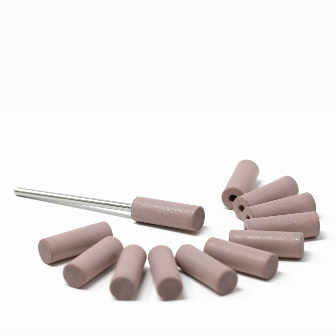 Set of twelve pink polishing cylinders on a white background; one has a mandrel attached.
